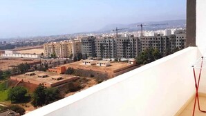 A view from a balcony overlooking a residential area with multiple apartment buildings, a clear sky, and distant mountains. - 2 bedroom apartment in agadir (Agadir)