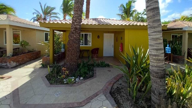 A yellow building with a tiled roof, surrounded by palm trees and a paved courtyard.
