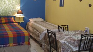 A room with two beds, a table, chairs, a ceiling fan, a wall clock, and an air conditioner.