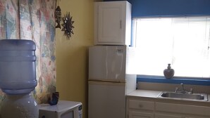 A kitchen with a refrigerator, microwave, water dispenser, and a window with blinds.