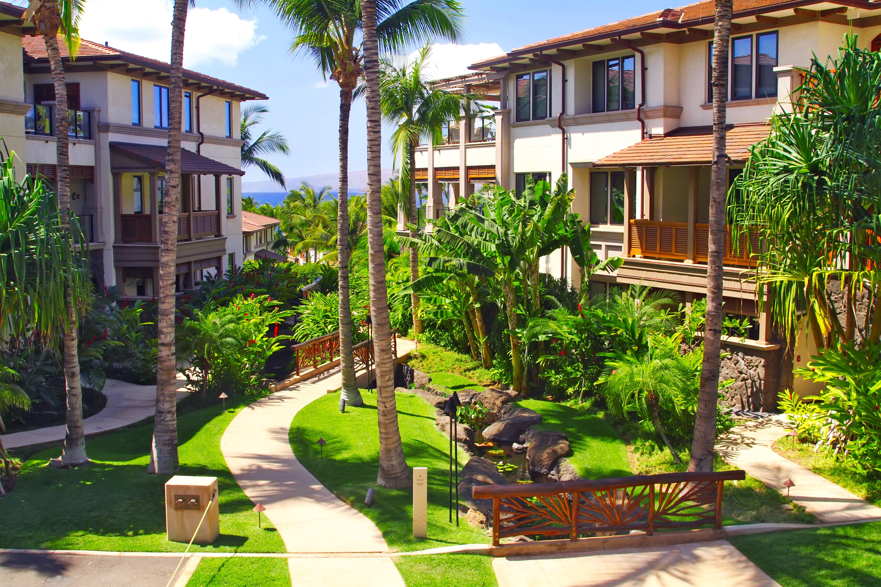 A resort with multiple-story buildings, palm trees, and a well-maintained garden with a pathway.