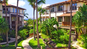 Een resort met meerlaags gebouwen, palmbomen en een verzorgde tuin met een pad.