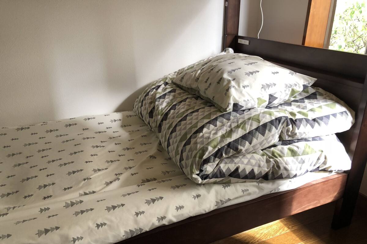 Ein Einzelbett mit gemustertem Bettbezug und Kissen, ein hölzernes Kopfteil und eine Steckdose an der Wand.