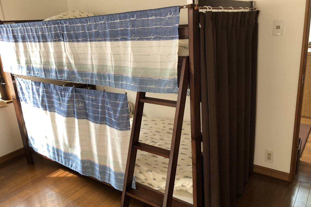 Ein Stockbett mit einer blau-weiß gestreiften Decke und einem dunkelbraunen Vorhang.