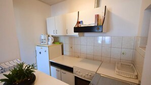 Ett kompakt kök med vita skåp, ett litet kylskåp, en kaffebryggare och en brödrost.