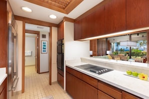 Una cocina moderna con armarios de madera, un refrigerador de acero inoxidable y un amplio ventanal con vistas a un paisaje tropical.