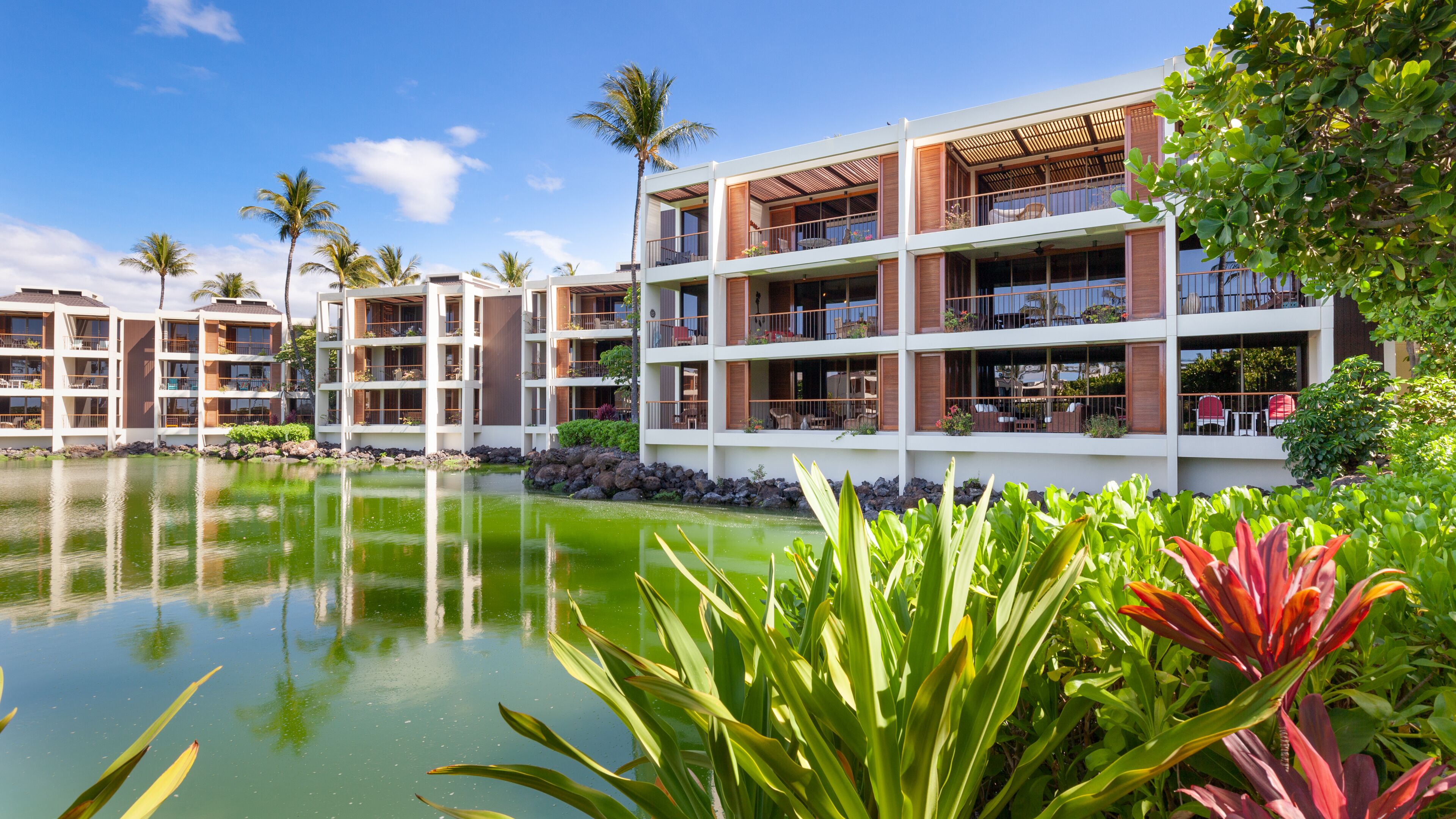 A multi-story hotel with balconies, a pool, and tropical landscaping.