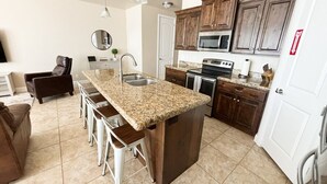 Une cuisine dotée de plans de travail en granit, d’un îlot central avec des tabourets de bar, de meubles en bois foncé, d’appareils électroménagers en acier inoxydable et d’une porte blanche.