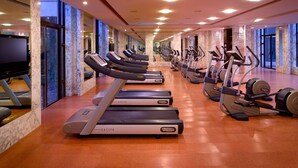 Un gimnasio con varias cintas de correr y máquinas elípticas, ventanas amplias y suelo de mármol.