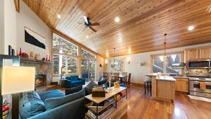 Un amplio salón con chimenea, un sofá azul y una cocina con armarios de madera y microondas.