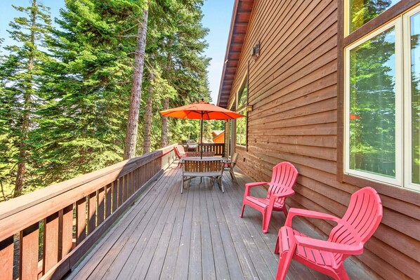 A wooden deck with a table and chairs, overlooking a forest.