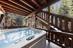 A hot tub on a wooden deck with a view of trees.