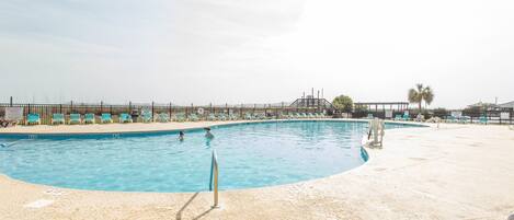 Une piscine avec une zone de plage de sable, des chaises longues et un poste de surveillance pour les sauveteurs.