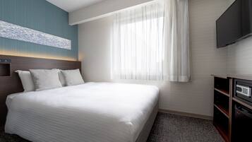 Habitación de hotel con una cama grande, un televisor de pantalla plana montado en la pared, una ventana con cortinas translúcidas y un cabecero de madera.