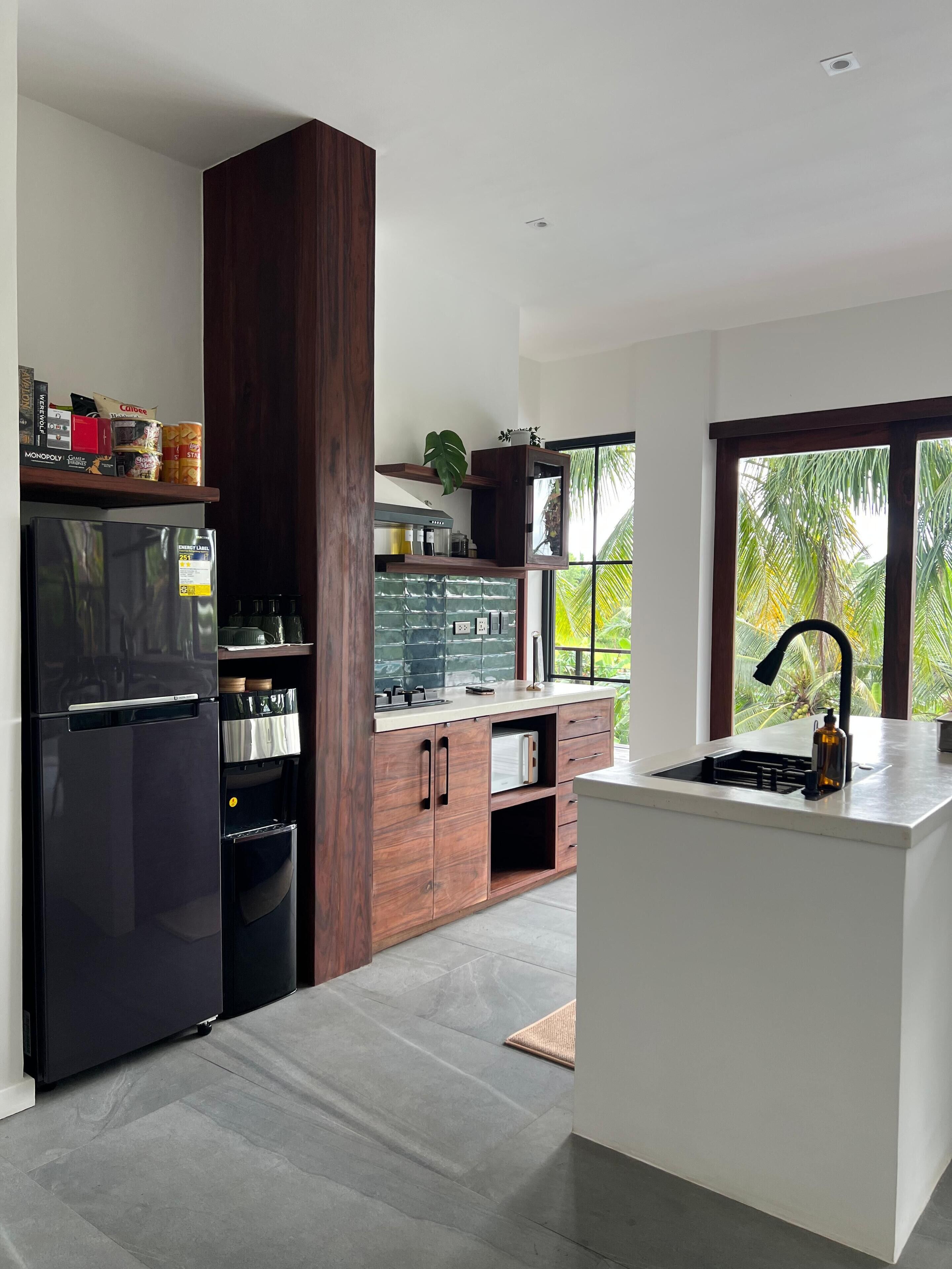 A modern kitchen with a built-in refrigerator, wooden cabinets, a countertop, and a window with a view of palm trees.