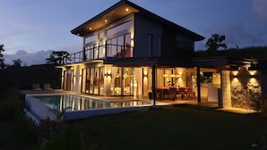 Una casa moderna de dos pisos con piscina, ventanas amplias y mobiliario exterior.