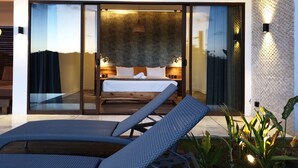 Un dormitorio moderno con una cama grande, puertas de cristal correderas que dan a un balcón y un pequeño rincón de descanso con una mesa y sillas.