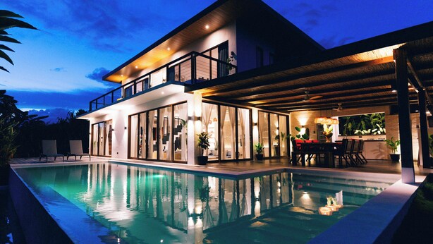 Una casa moderna de dos pisos con piscina, ventanas amplias y un espacio exterior cubierto.