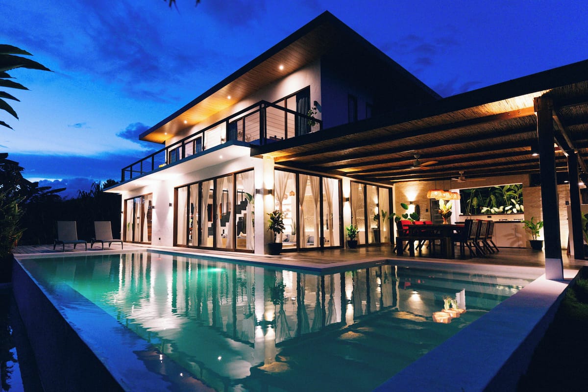 A modern two-story house with a swimming pool, large windows, and a covered outdoor area.