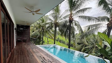 Una terraza de madera con piscina, rodeada de palmeras y un ventilador de techo.