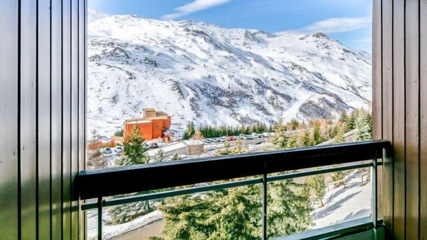 A mountain view from a window with a wooden frame, a small building, and a parking area.