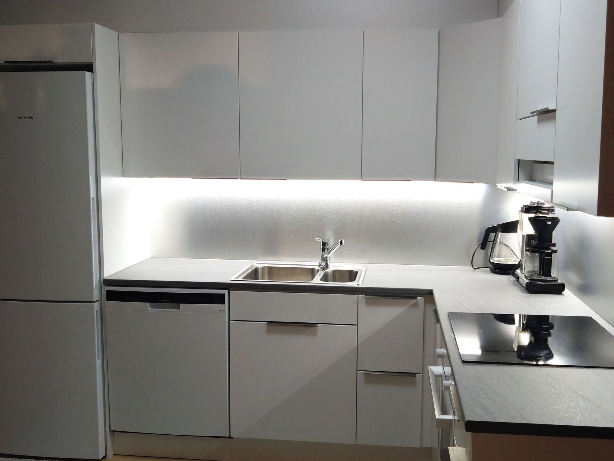 A modern kitchen with a built-in dishwasher, a double sink, and a coffee machine.