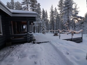A log cabin with a snow-covered roof, surrounded by a forest.