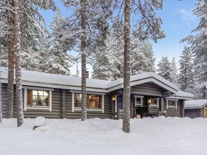 A log cabin with multiple windows and a visible door, surrounded by snow-covered trees.