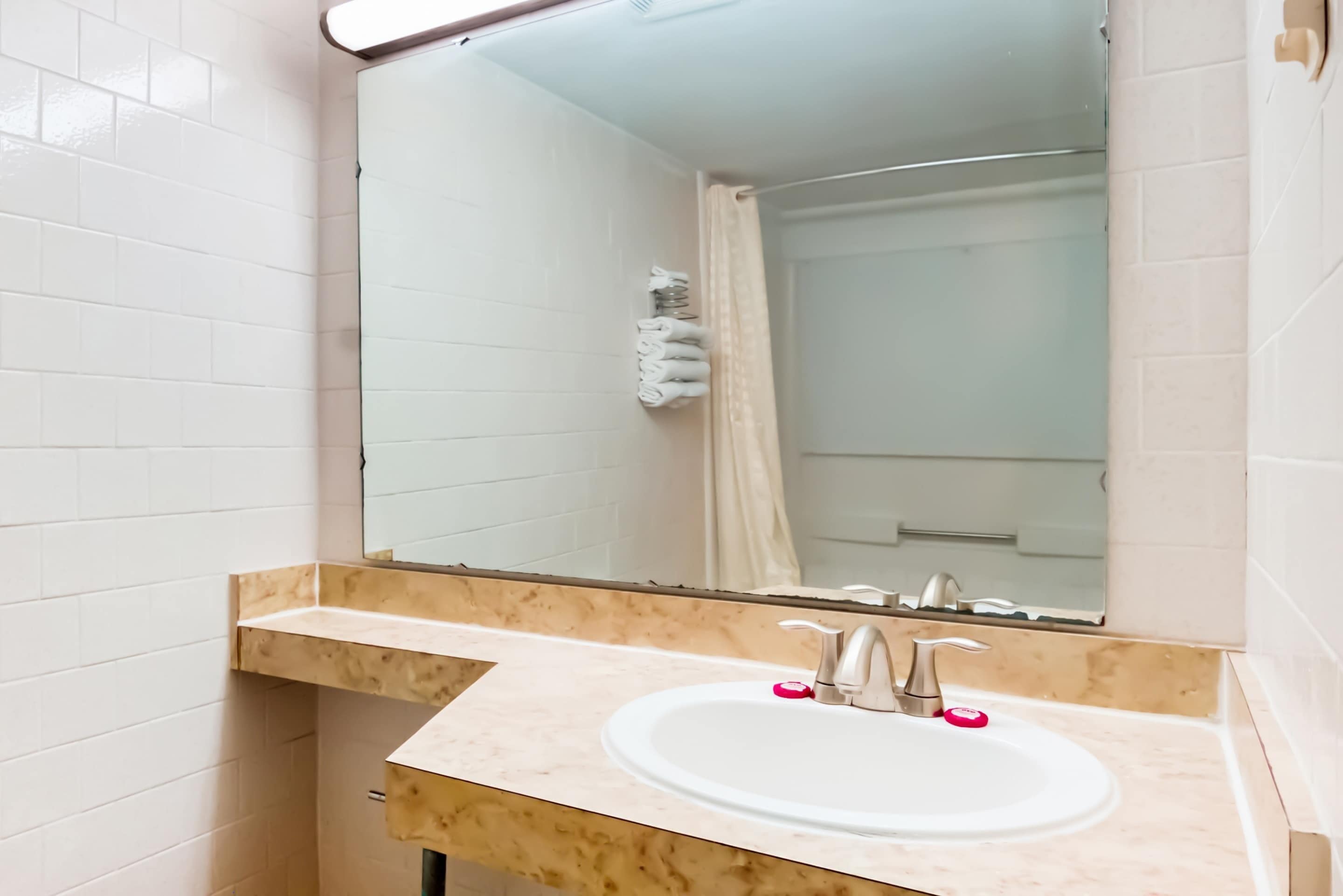 Een badkamer met een wit wastafel, een spiegel en een douche die op de achtergrond zichtbaar is.