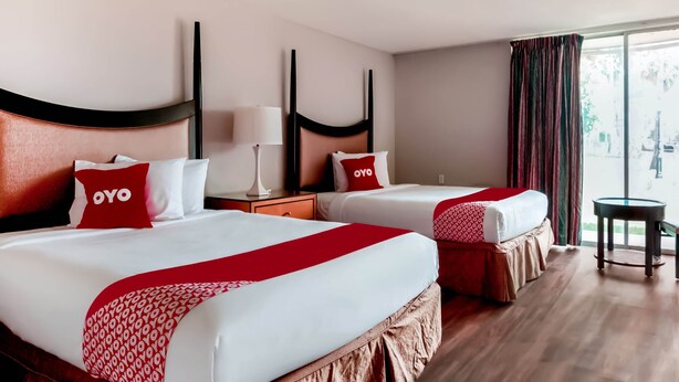 A hotel room with two beds, each with a red and white bedspread, a headboard, and a nightstand with a lamp. - OYO Hotel Alice TX Hwy 281 West (Alice)