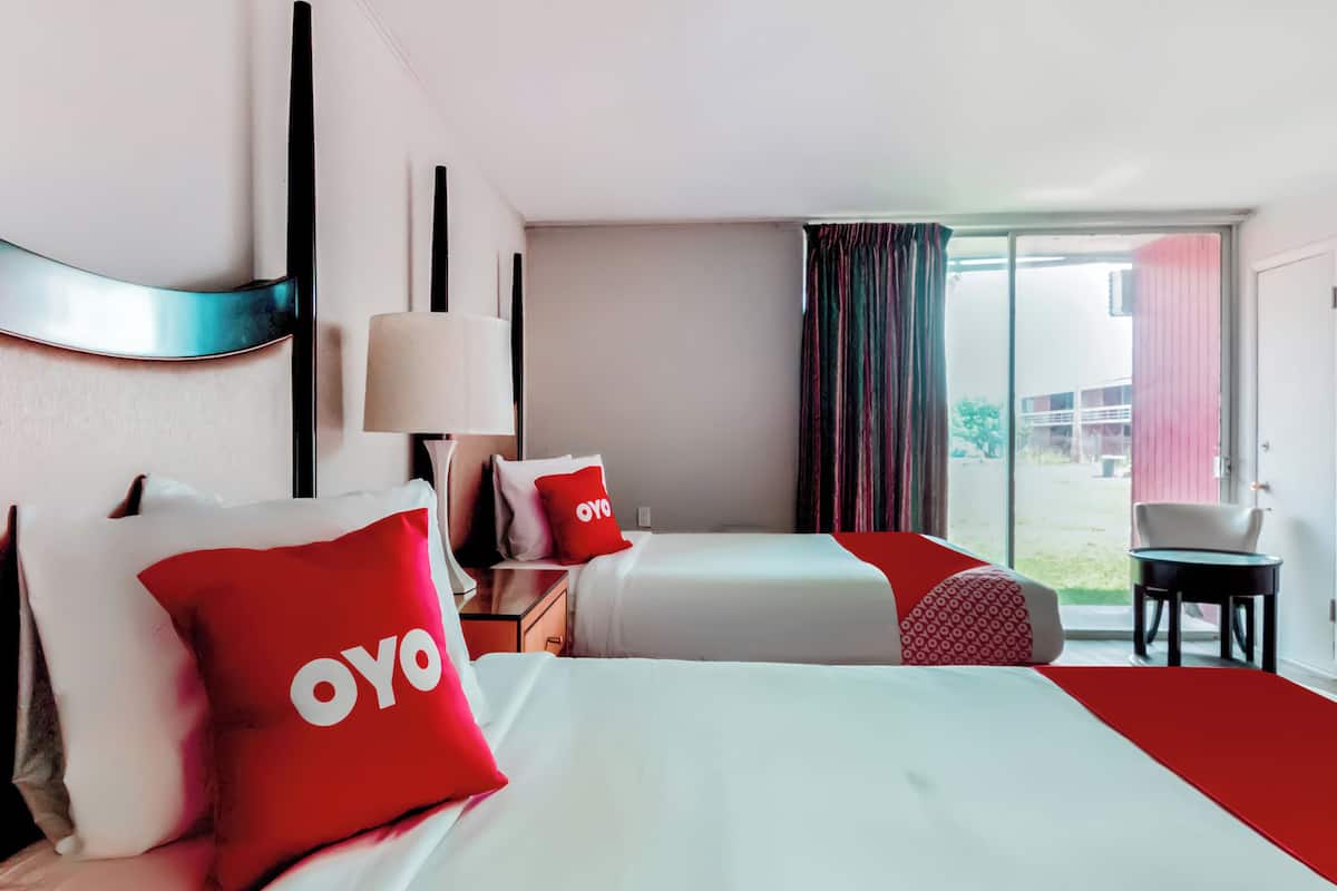 Une chambre d’hôtel avec deux lits, un oreiller rouge de la marque OYO, une lampe, une chaise et une vue sur l’extérieur.
