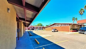 A parking area with blue painted lines, a covered walkway, and a building with a brick facade. - OYO Hotel Alice TX Hwy 281 West (Alice)