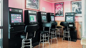 A bar area with four gaming machines, black bar stools, and framed pictures on the wall. - OYO Hotel Alice TX Hwy 281 West (Alice)