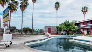 A swimming pool area with a sign for 'Scottish Inns' and a building with a red door and windows. - OYO Hotel Alice TX Hwy 281 West (Alice)