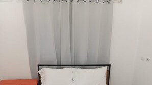 A bed with white bedding, a rainbow-striped blanket, and a blue plush toy.
