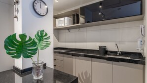 Ett modernt kök med vita skåp, en svart bänkskiva, en klocka och en krukväxt av sorten monstera.