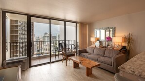 Ein großzügiges Wohnzimmer mit einer großen Schiebeglasdoor zum Balkon, einer Couch, einem Holztisch und einem kleinen Beistelltisch mit Lampe und Dekoration.