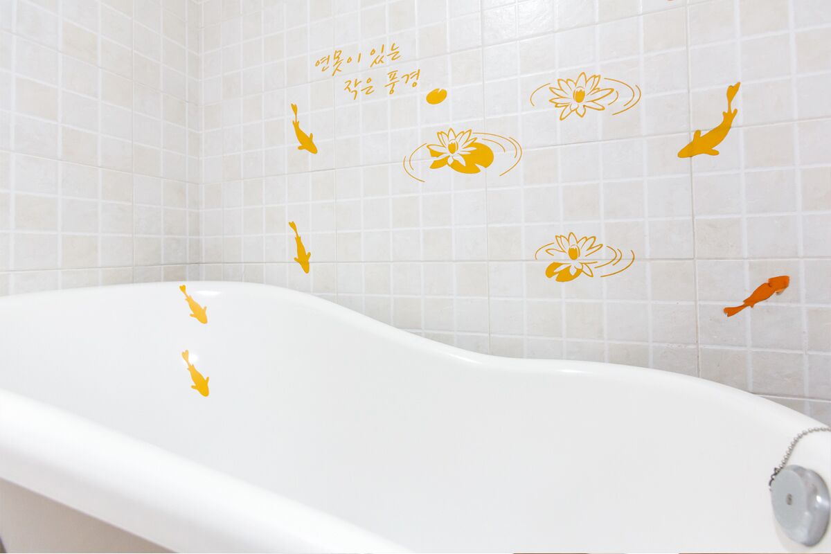 A bathtub with a white interior and a tiled wall with decorative fish and lotus flower decals.