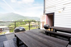 Una terraza de madera con una parrilla y bancos, con vista a un paisaje montañoso.