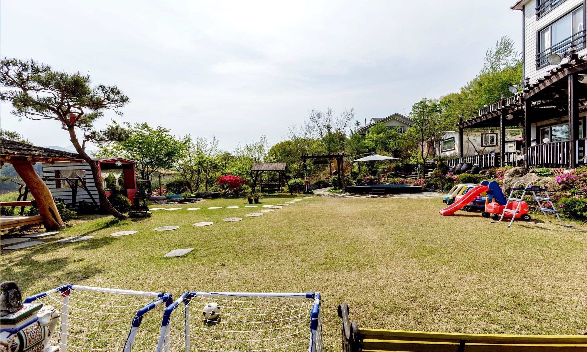 Ein Garten mit Rasen, einem Fußballtor, einer Rutsche und einer Pergola.