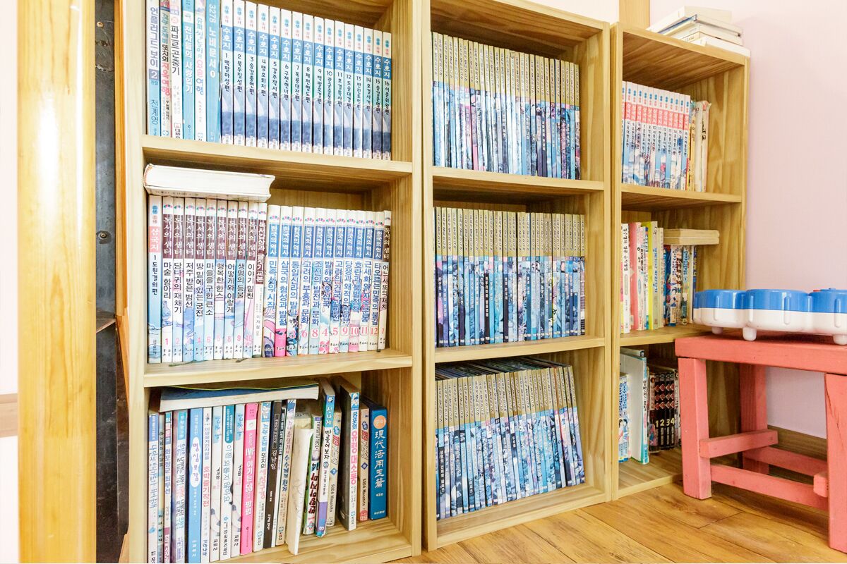 A bookshelf filled with books in a room with wooden flooring and a pink table.
