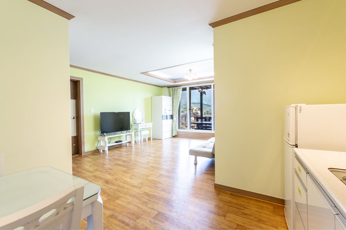 A spacious living room with a wooden floor, a flat-screen TV, a dining table, and a sofa.