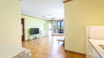 A spacious living room with a wooden floor, a flat-screen TV, a dining table, and a sofa.