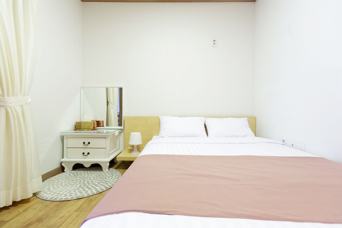 A bedroom with a bed, a nightstand, a lamp, a mirror, and a pet bed.