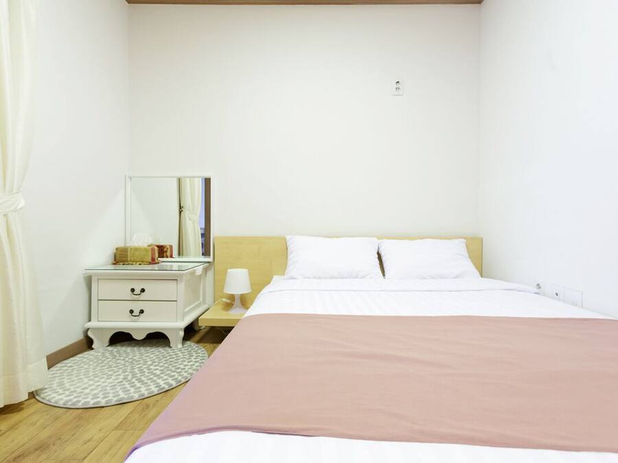 A bedroom with a bed, a nightstand, a lamp, a mirror, and a pet bed.