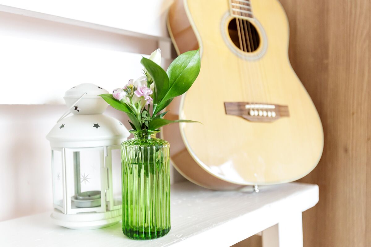 A white shelf with a green vase and a white lantern. A guitar is visible in the background.