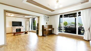 A spacious living room with a fireplace, a piano, and large windows offering a view of the outdoors.