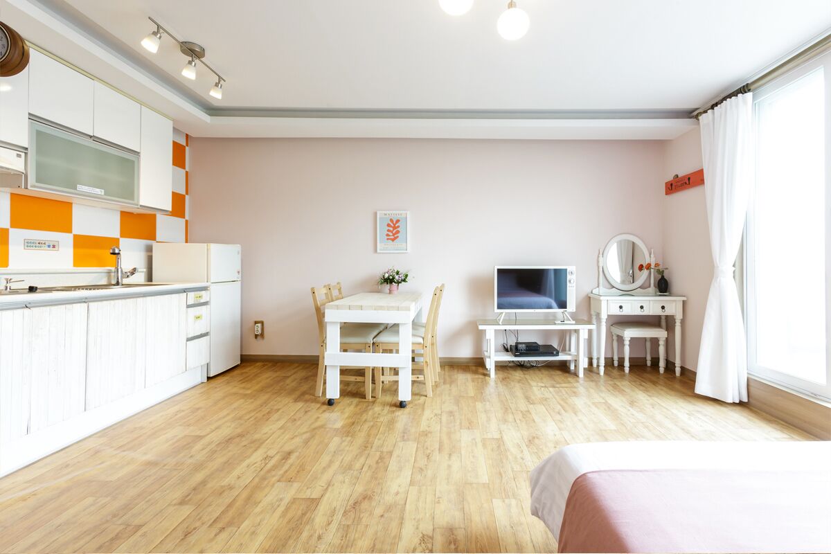 A modern hotel room with a kitchen, a dining area, and a TV.
