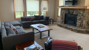 A living room with a stone fireplace, large windows, and a television mounted above it.