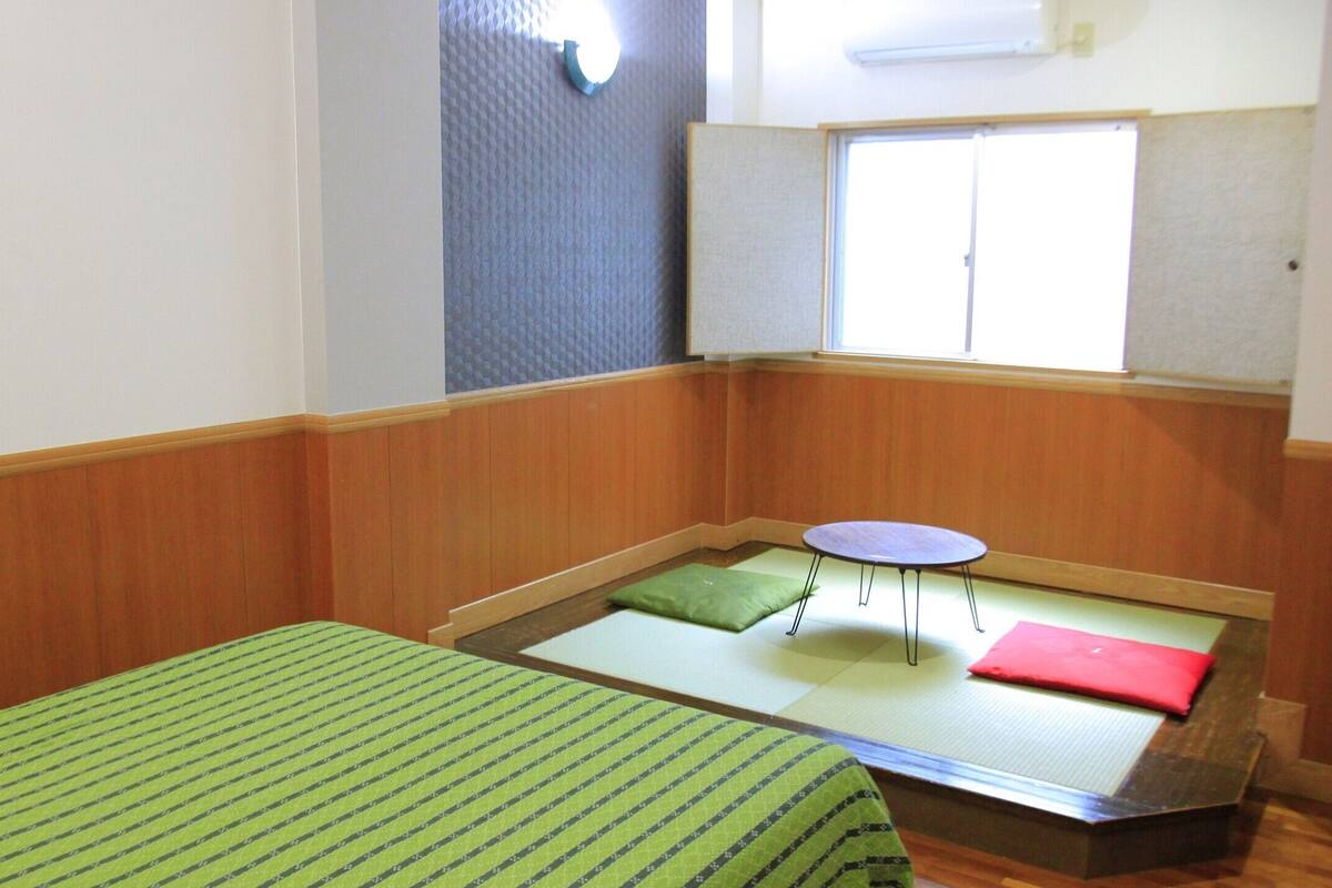 Una habitación con dos camas, una mesita y un ventanal.